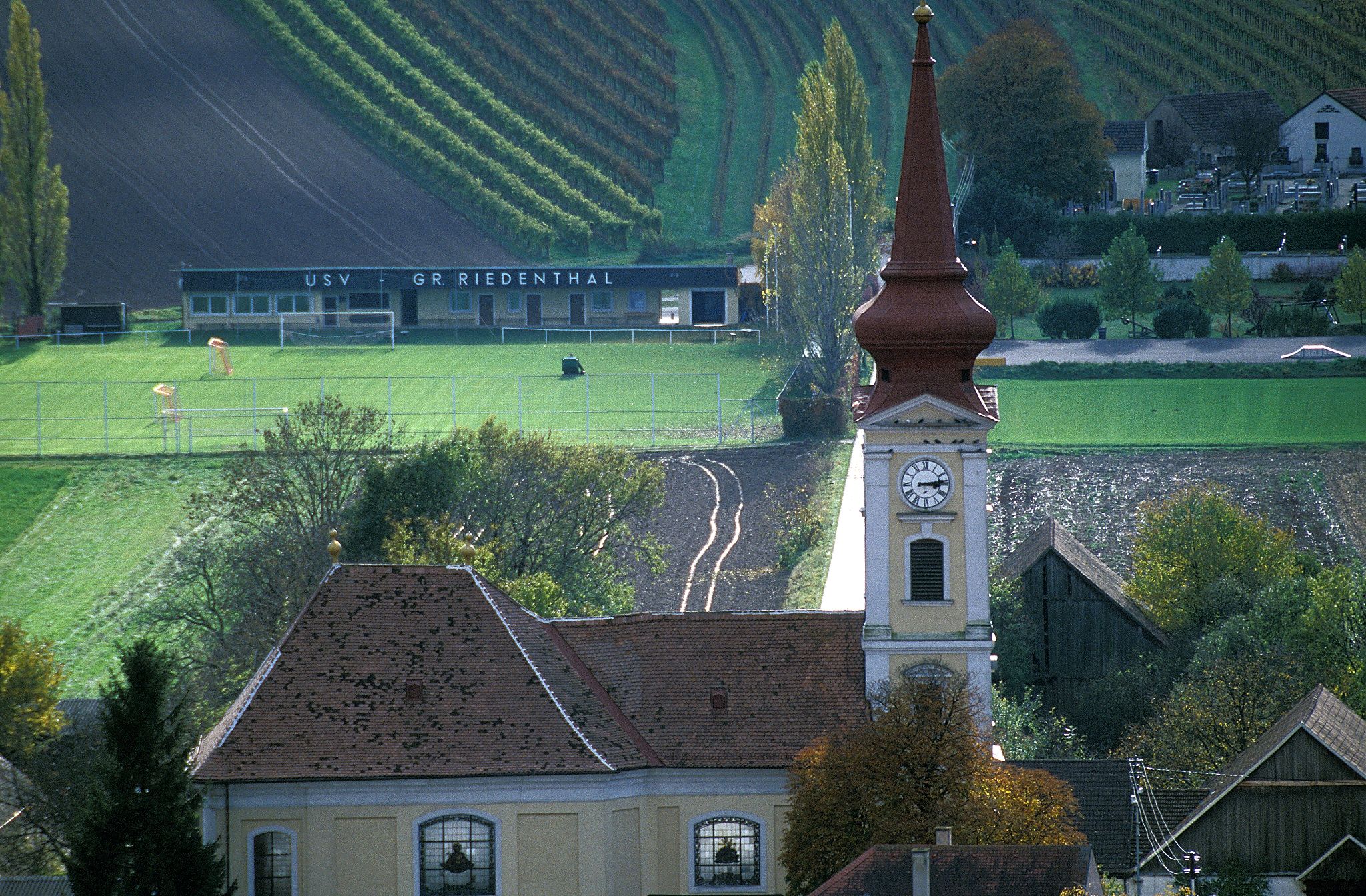 Großriedenthal parish church with church tower and surrounding fields and buildings.