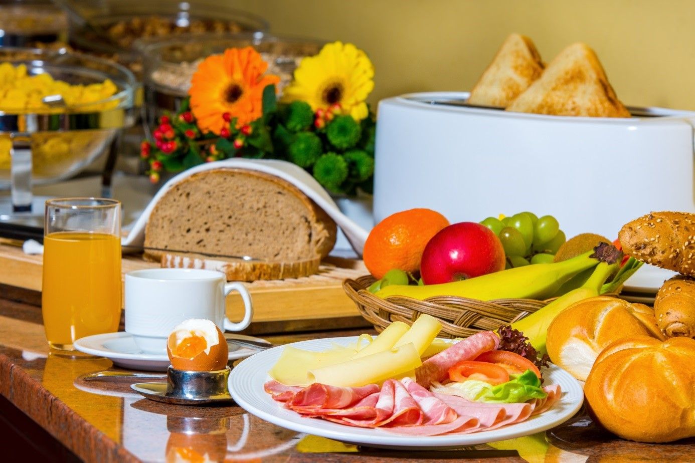 Breakfast buffet with bread, cold cuts, cheese, fruit, rolls, juice and egg.