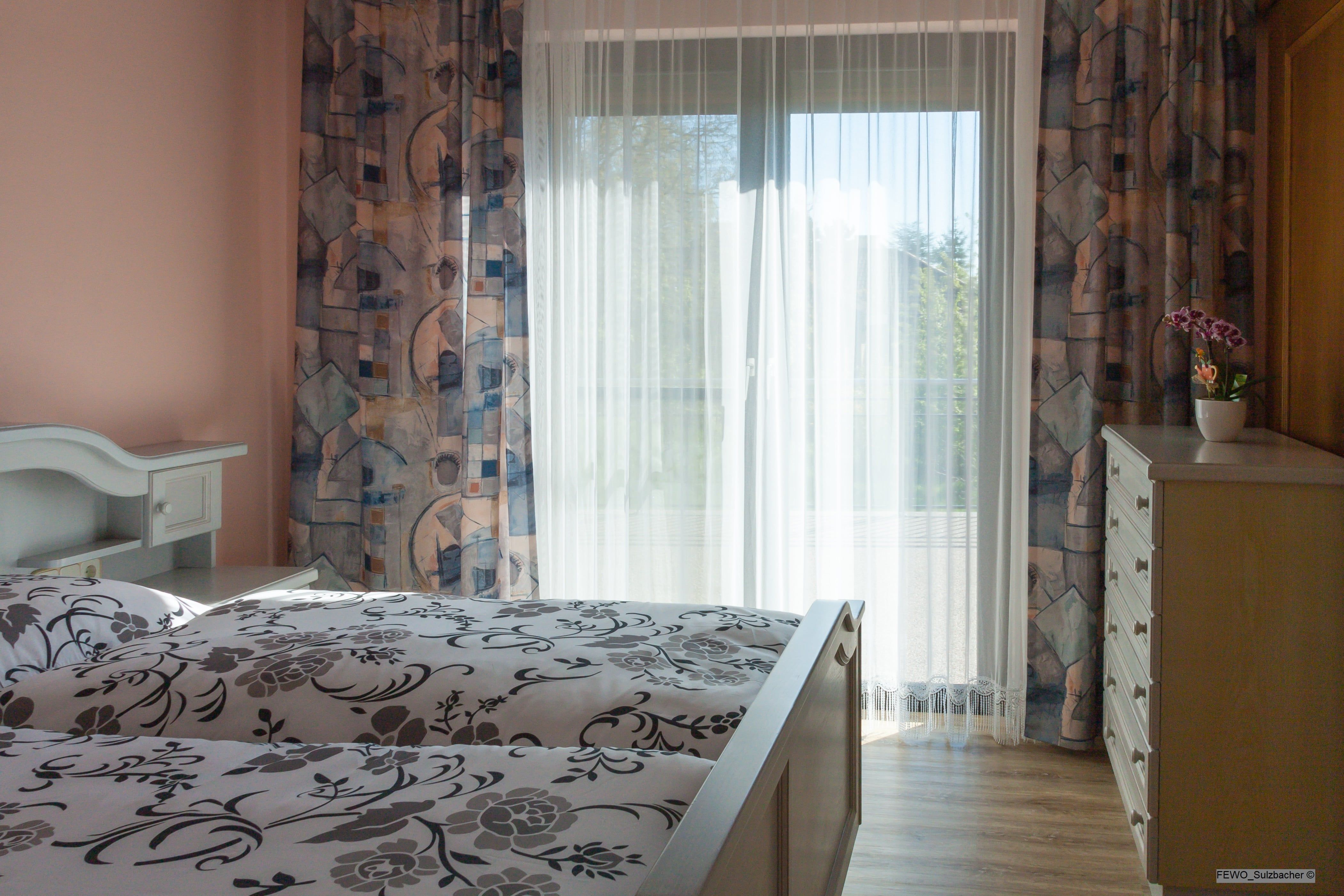Bright bedroom with bed, curtains and chest of drawers.