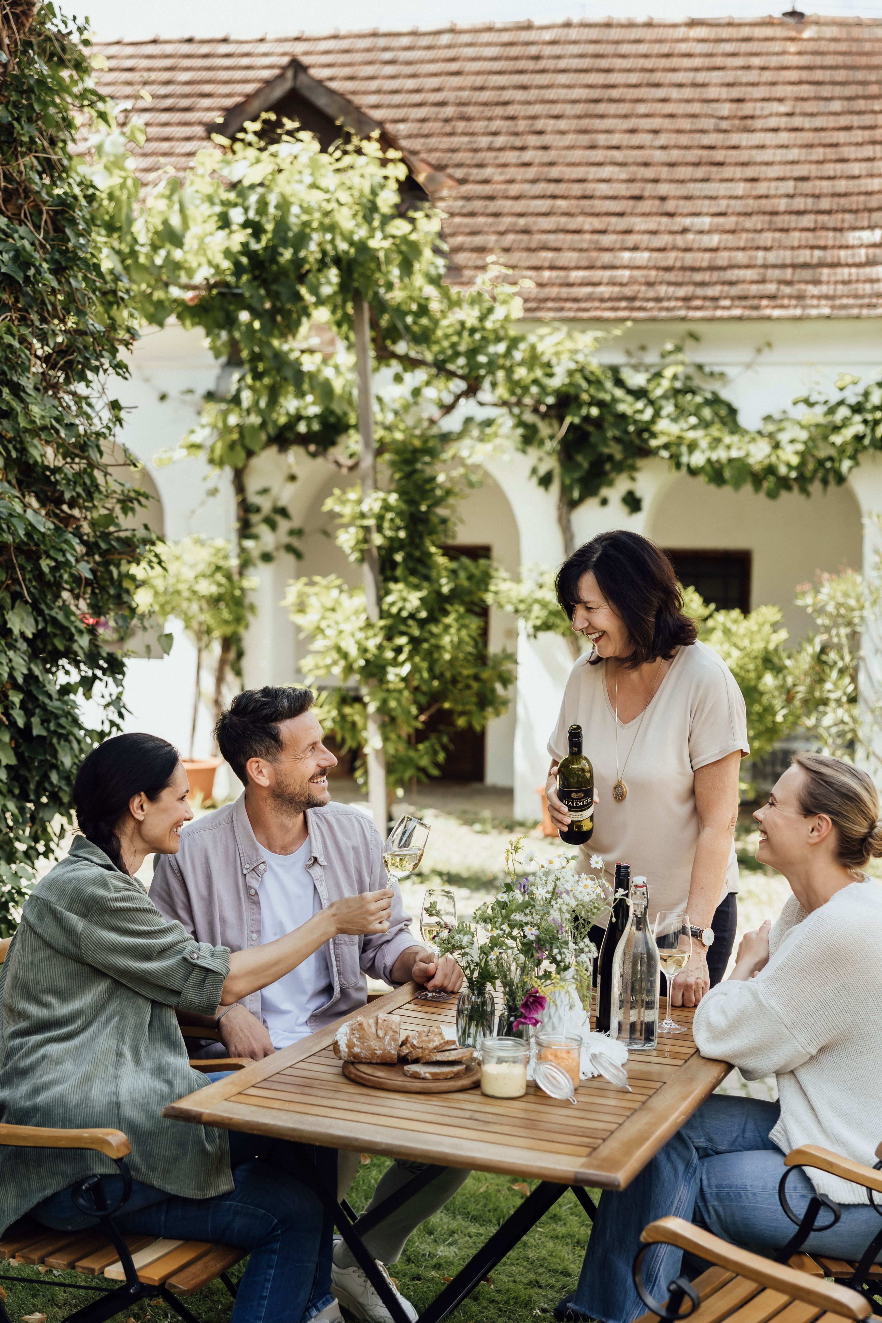 Four people sit at an outdoor table and enjoy wine and bread.