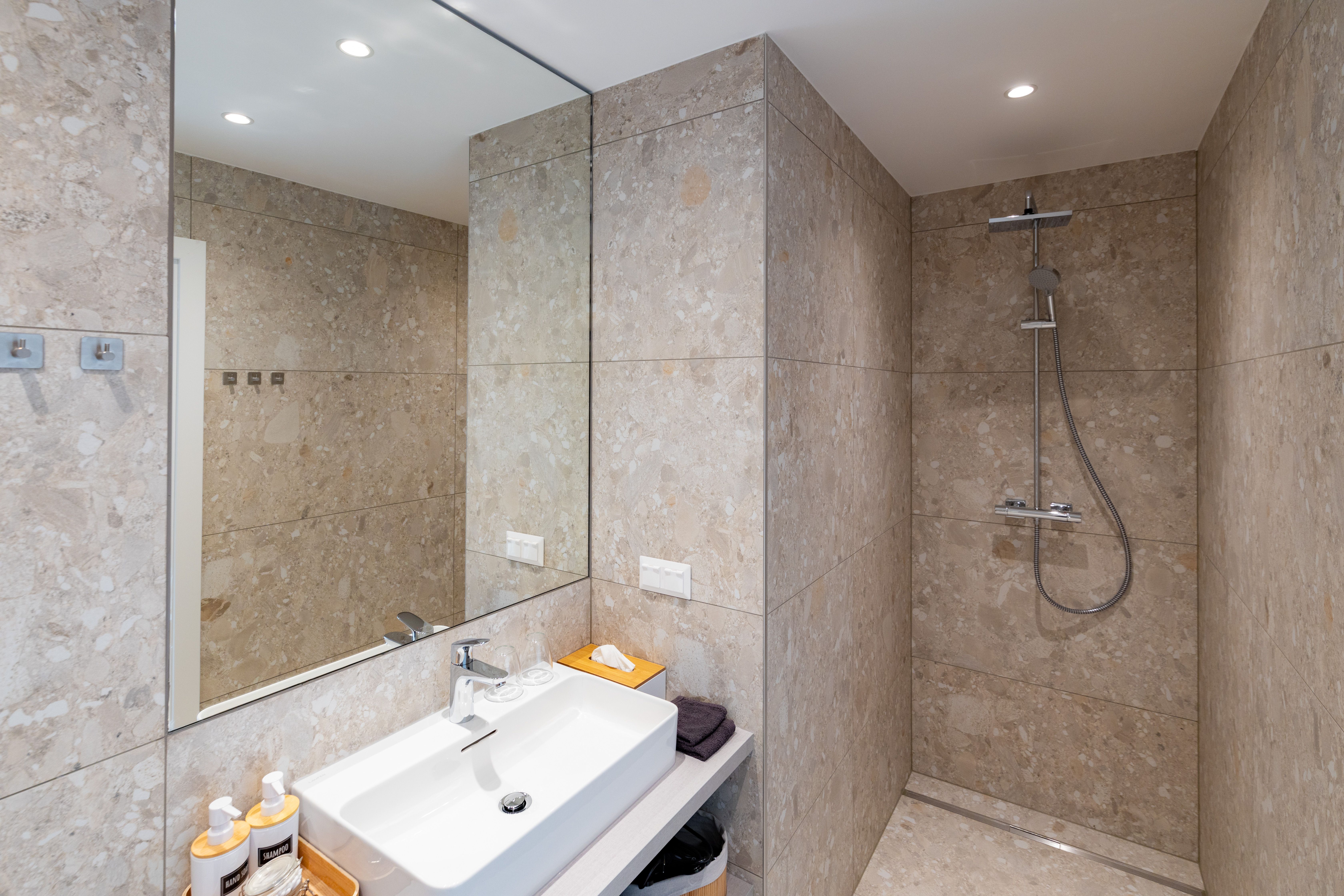 Modern bathroom with beige tiled wall, washbasin, mirror and rain shower.