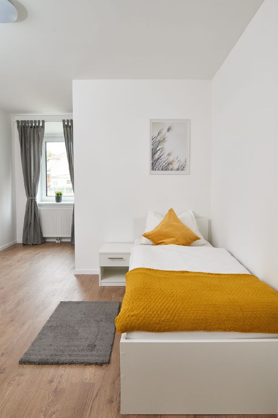 Single room with bed, bedside table and window with curtains.