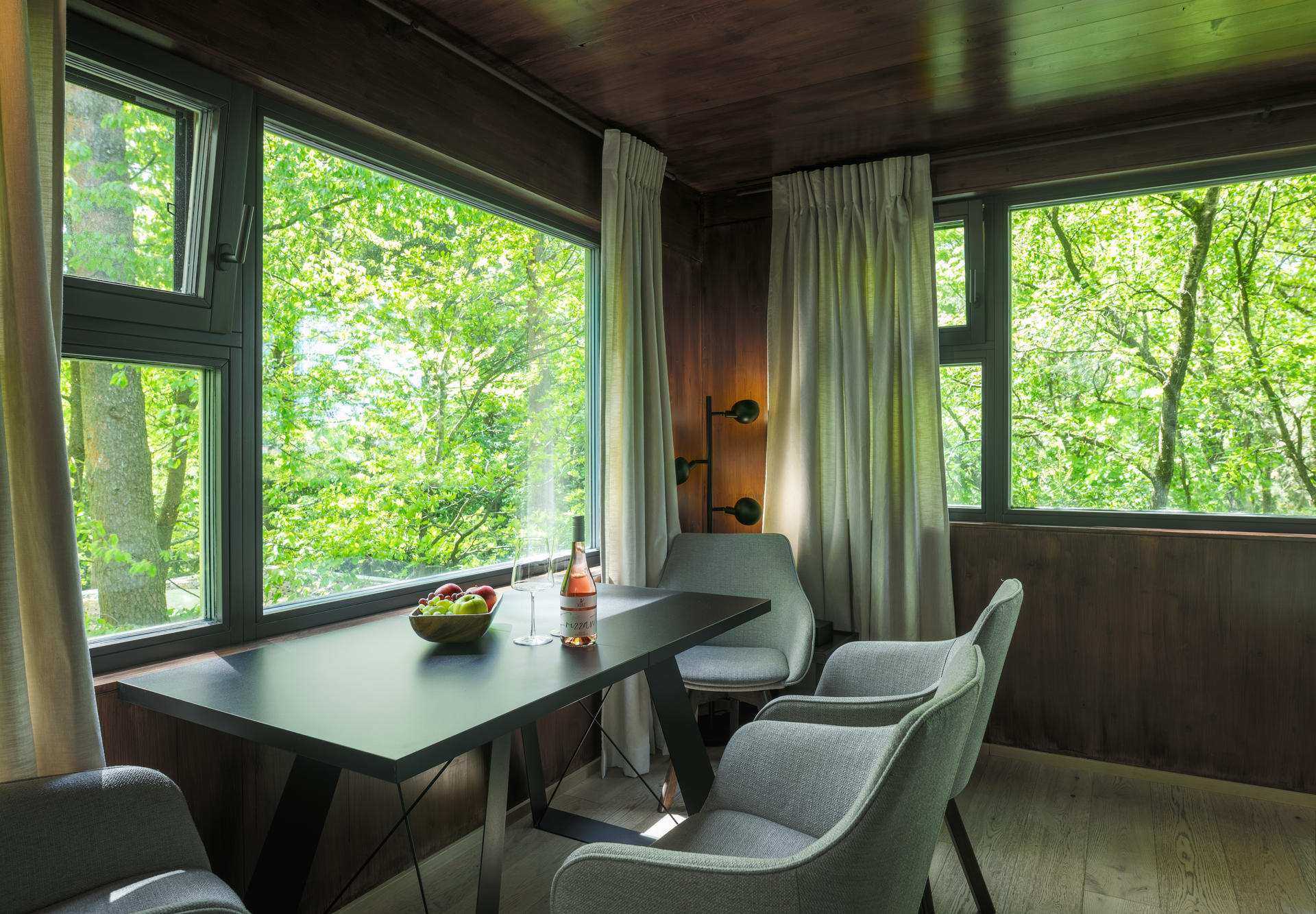 Interior view of a modern tree house with table, chairs and large windows with a view of the greenery.