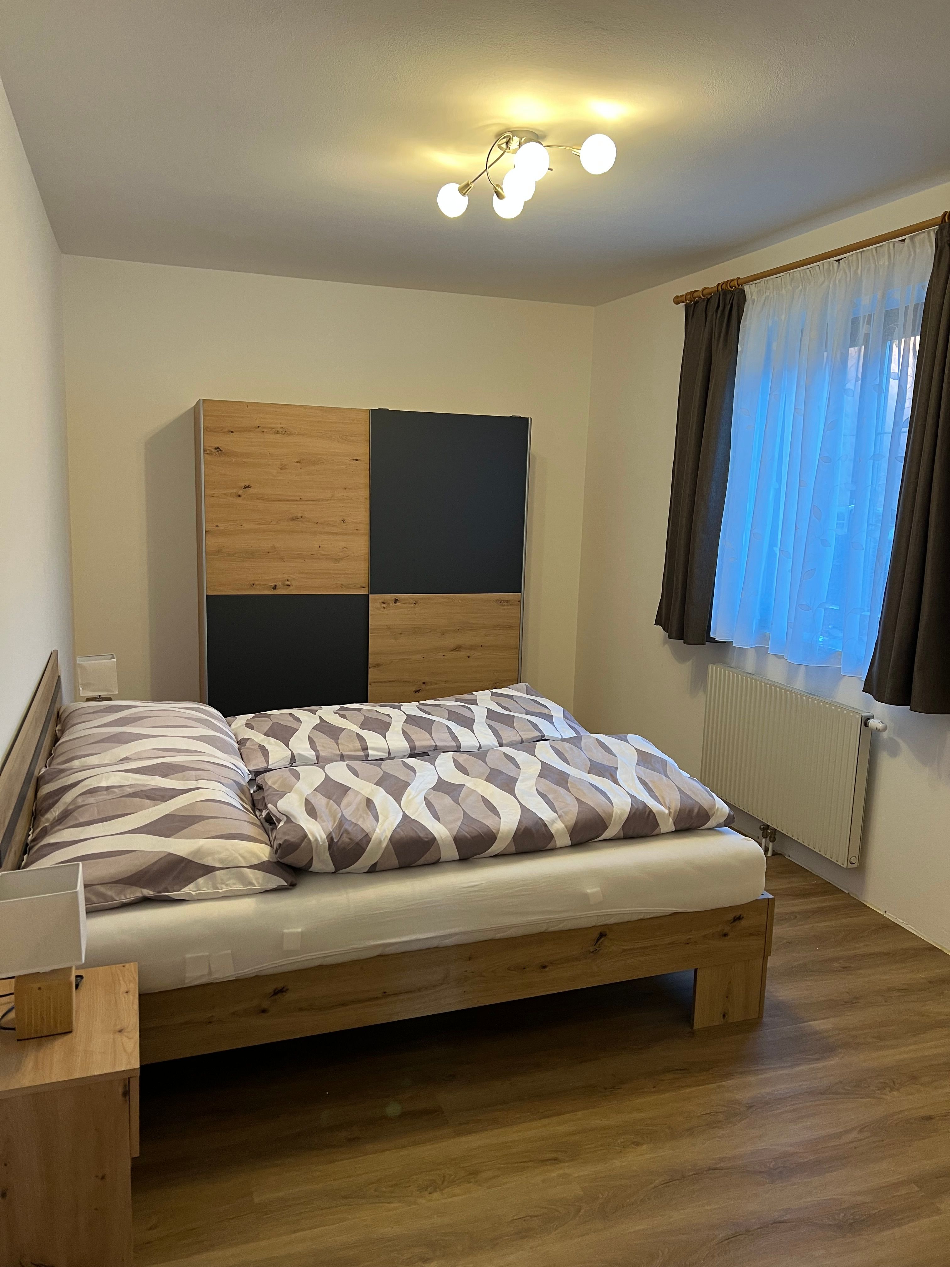 A cozy double room with a wooden bed, a closet and a window with curtains.