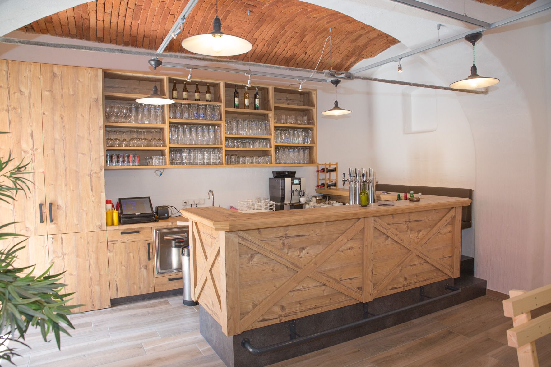Wooden bar with glasses and bottles and brick ceiling.