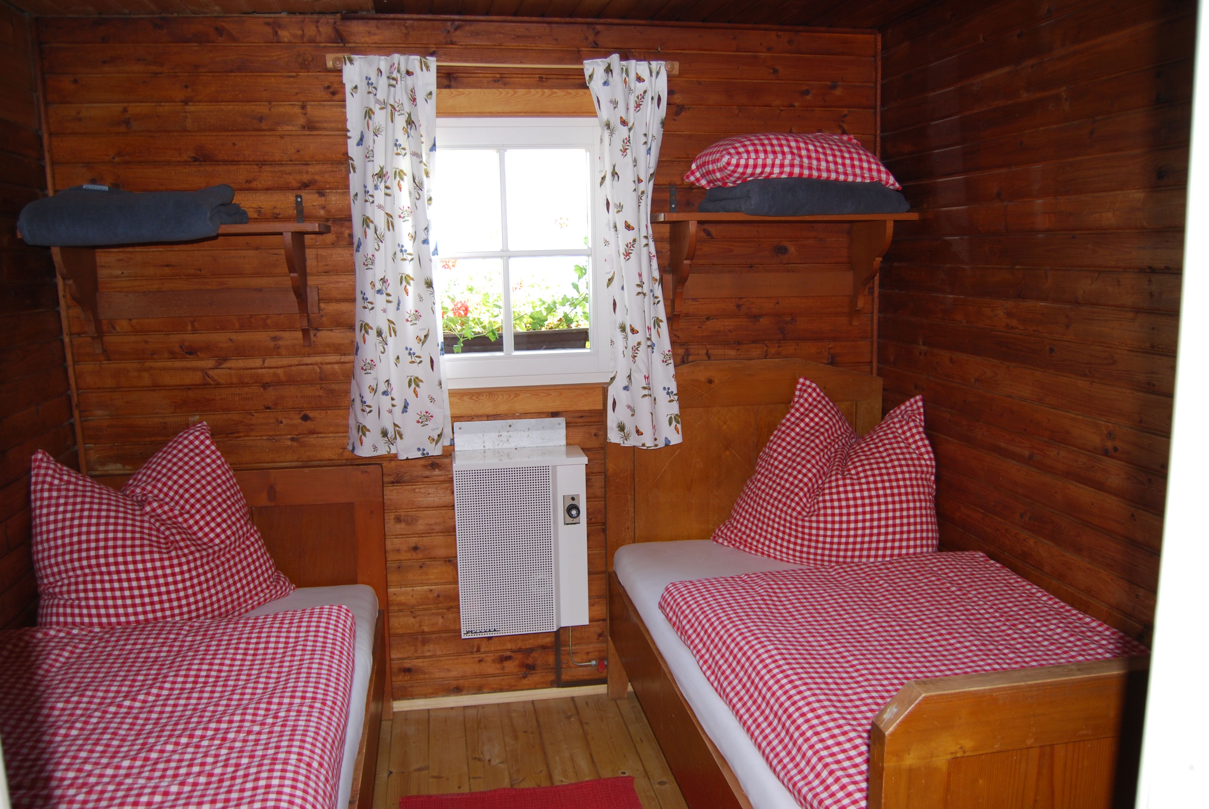 Wood-paneled room with two single beds, red and white checkered bedspreads and a window with flower curtains.
