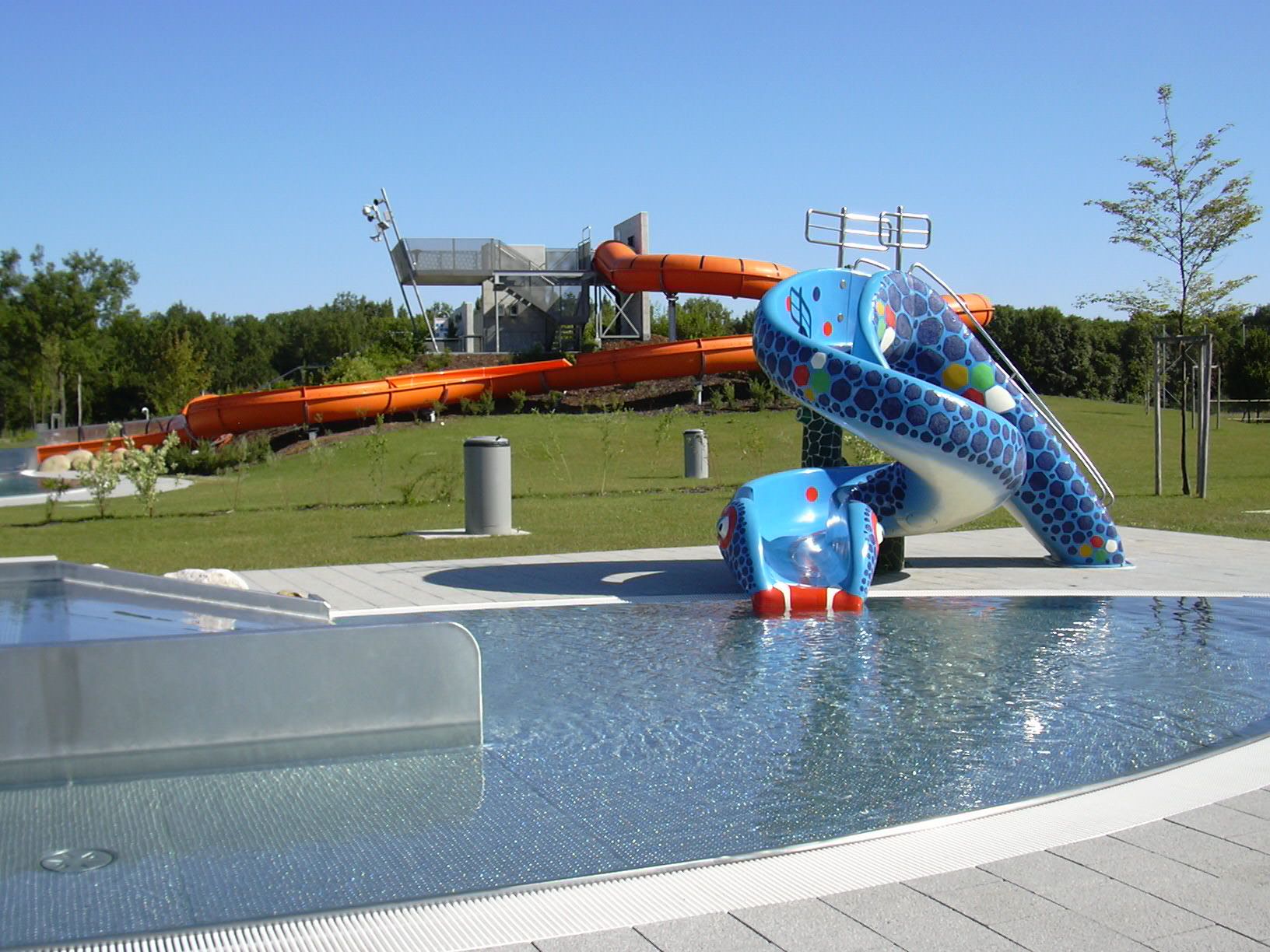 View of an aqua park with a blue children's slide and a large orange water slide in the background.