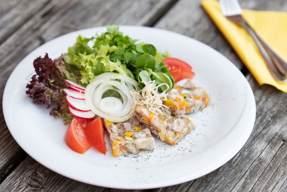 A plate of sausage, lettuce, tomatoes, radishes and onions on a wooden table.