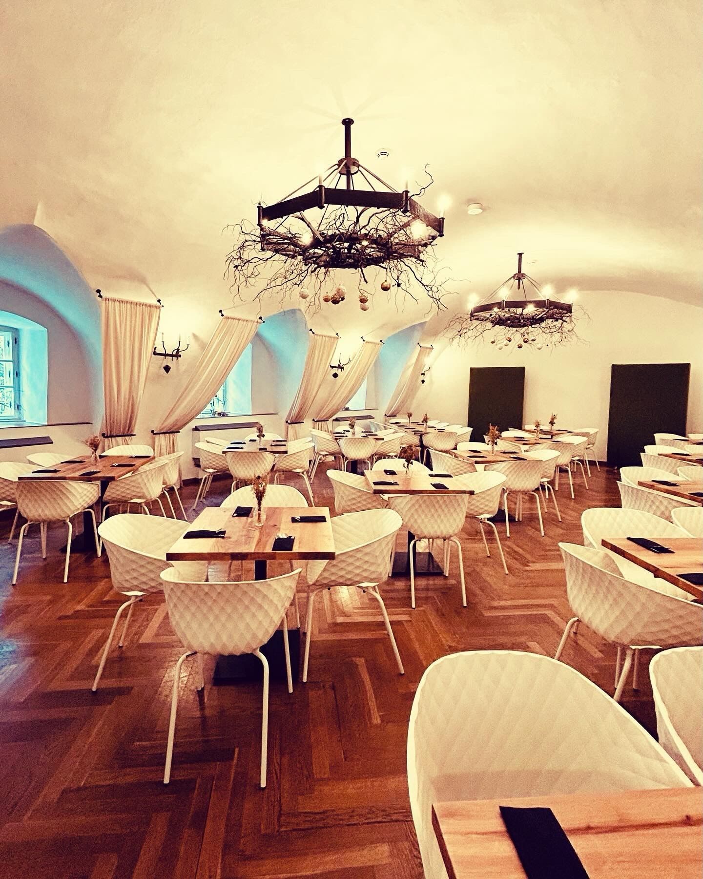Elegant dining room with parquet floor, white chairs, wooden tables and decorative chandeliers.
