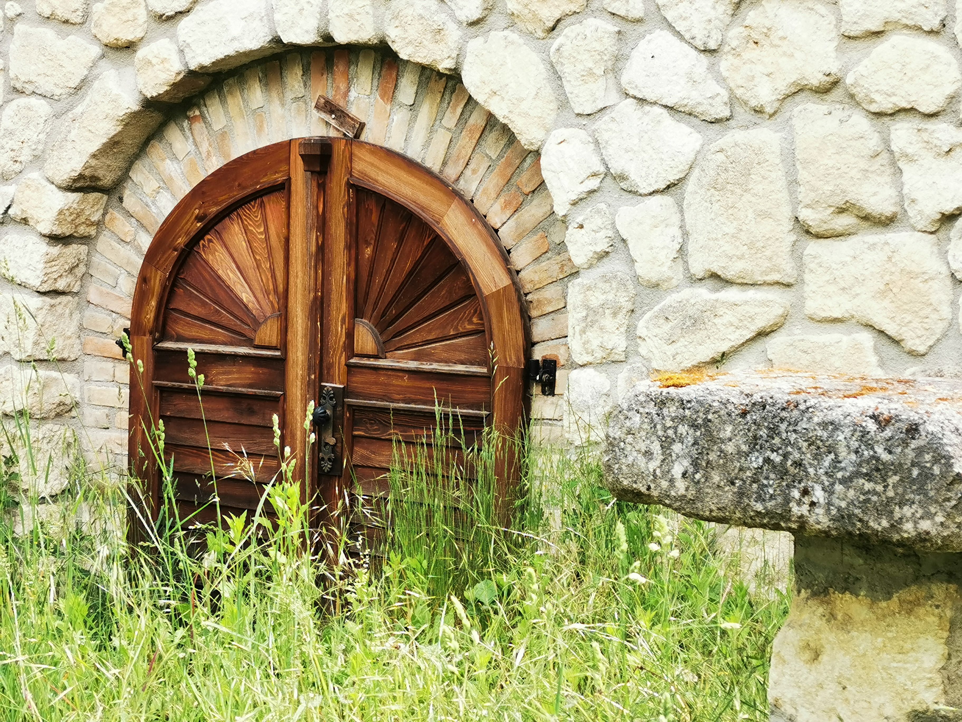 Wooden door in stone wall with grass in the foreground.