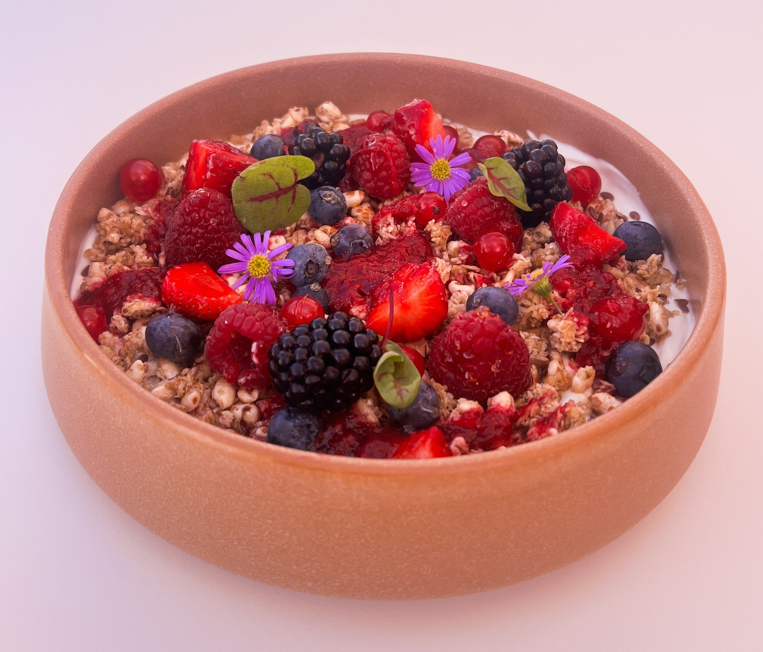 Bowl with yogurt, muesli, berries and edible flowers.