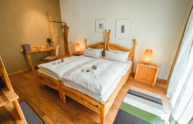 A cozy bedroom with wooden furniture, a double bed, bedside tables and a desk. Two lamps and pictures on the wall complete the ambience.