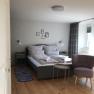 Modern furnished double room with bed, armchair and small table on wooden floor.