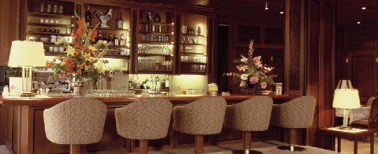 Elegant bar with wooden paneling, flower arrangements and upholstered bar stools.