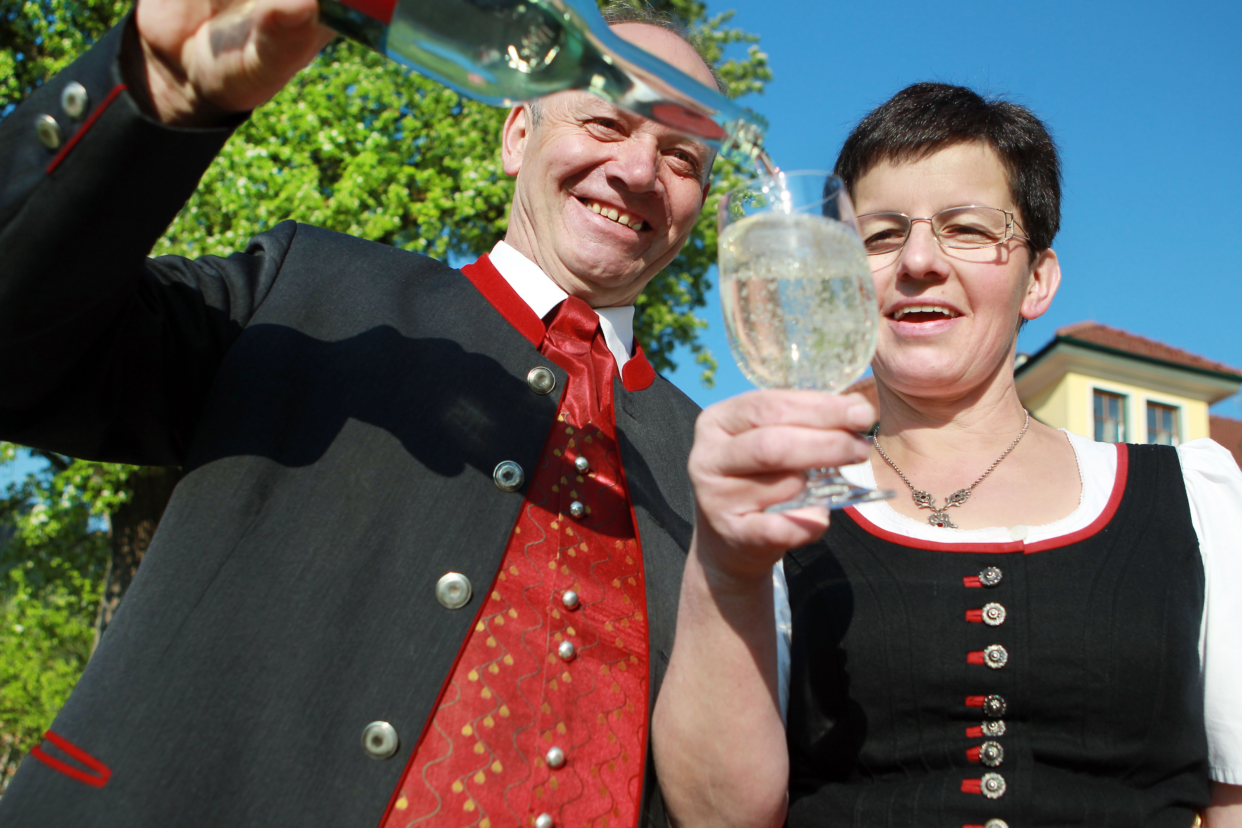 Two people in traditional dress clink glasses while a bottle is poured.