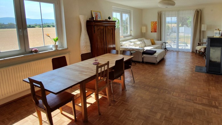 Bright room with dining table, chairs, sofa and large windows overlooking the countryside.