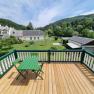 View from a balcony onto a garden with a green meadow and trees, with a large house and hills in the background.