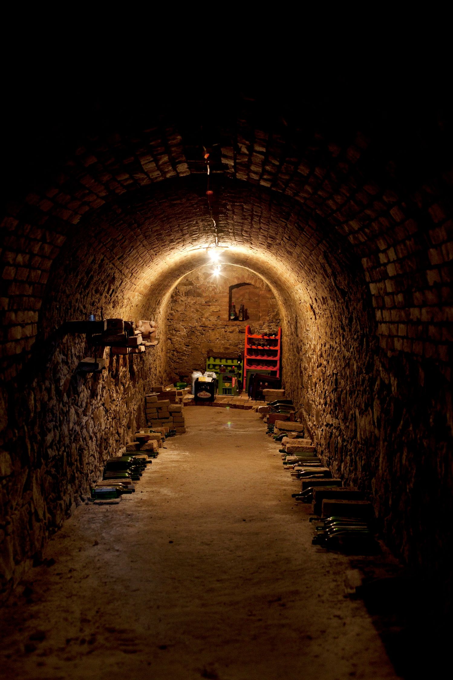 A narrow, vaulted wine cellar with brick walls and stored bottles.