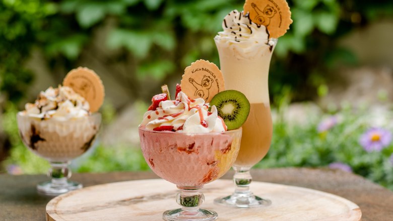 Three ice cream desserts on an outdoor table, decorated with cream, fruit and waffles.