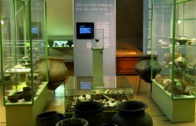 Museum exhibition with antique clay vessels and display cases.