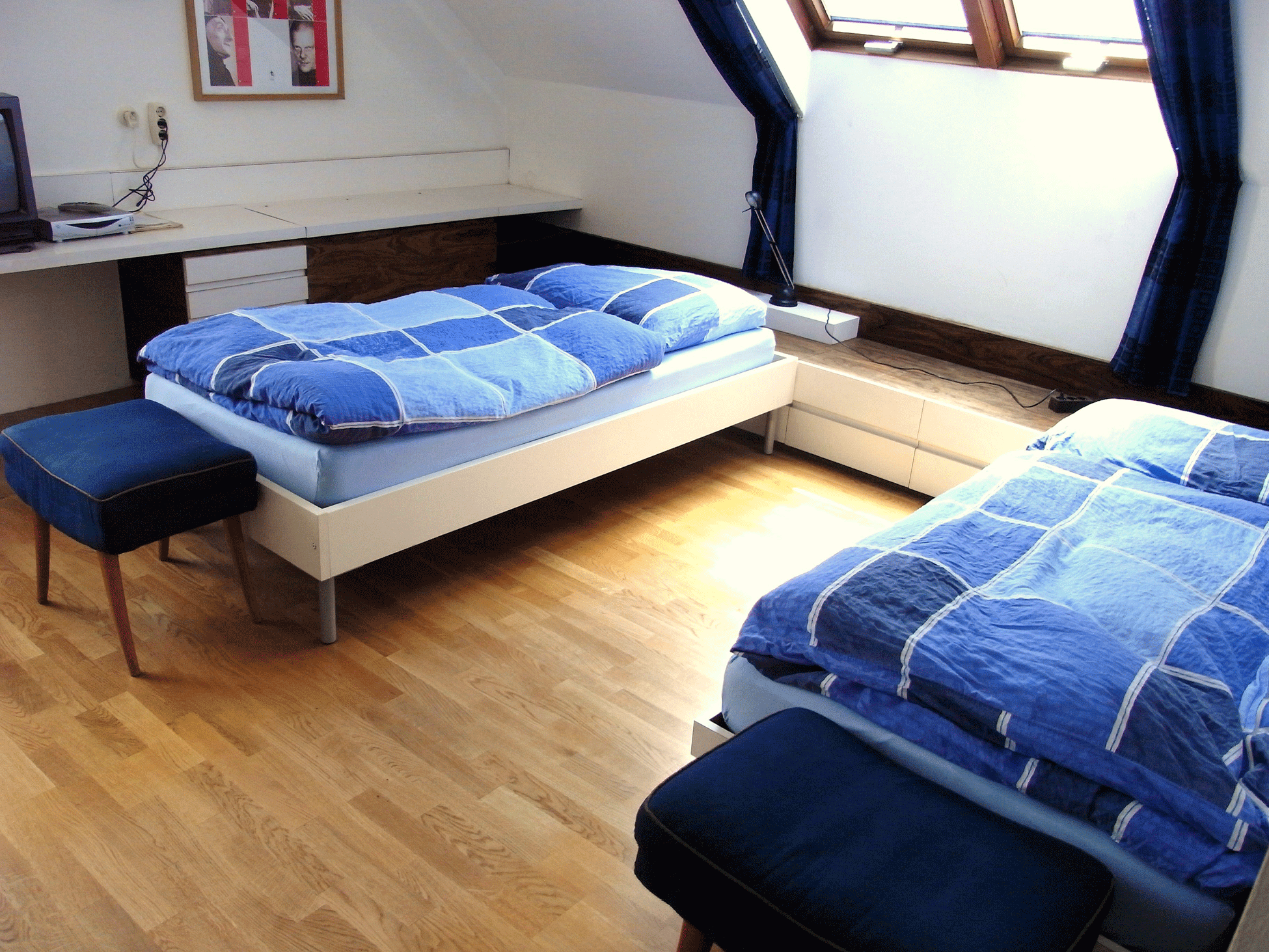 A bright bedroom with two single beds, blue comforters and a skylight.