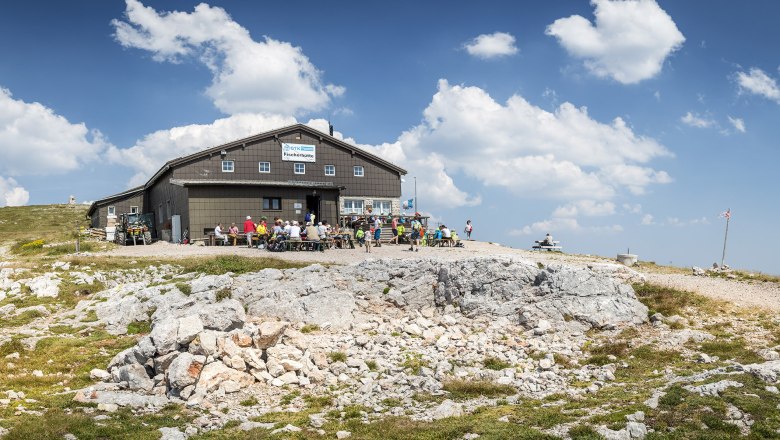 Fisherman's hut on the Schneeberg with hikers and a blue sky.