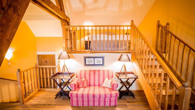 Cozy suite with wooden beams, staircase, sofa and lamps.