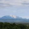 View of a landscape with wooded hills and a snow-capped mountain in the background.