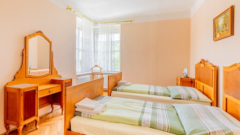 A traditional bedroom with two single beds, a dressing table with mirror and a window with white curtains.