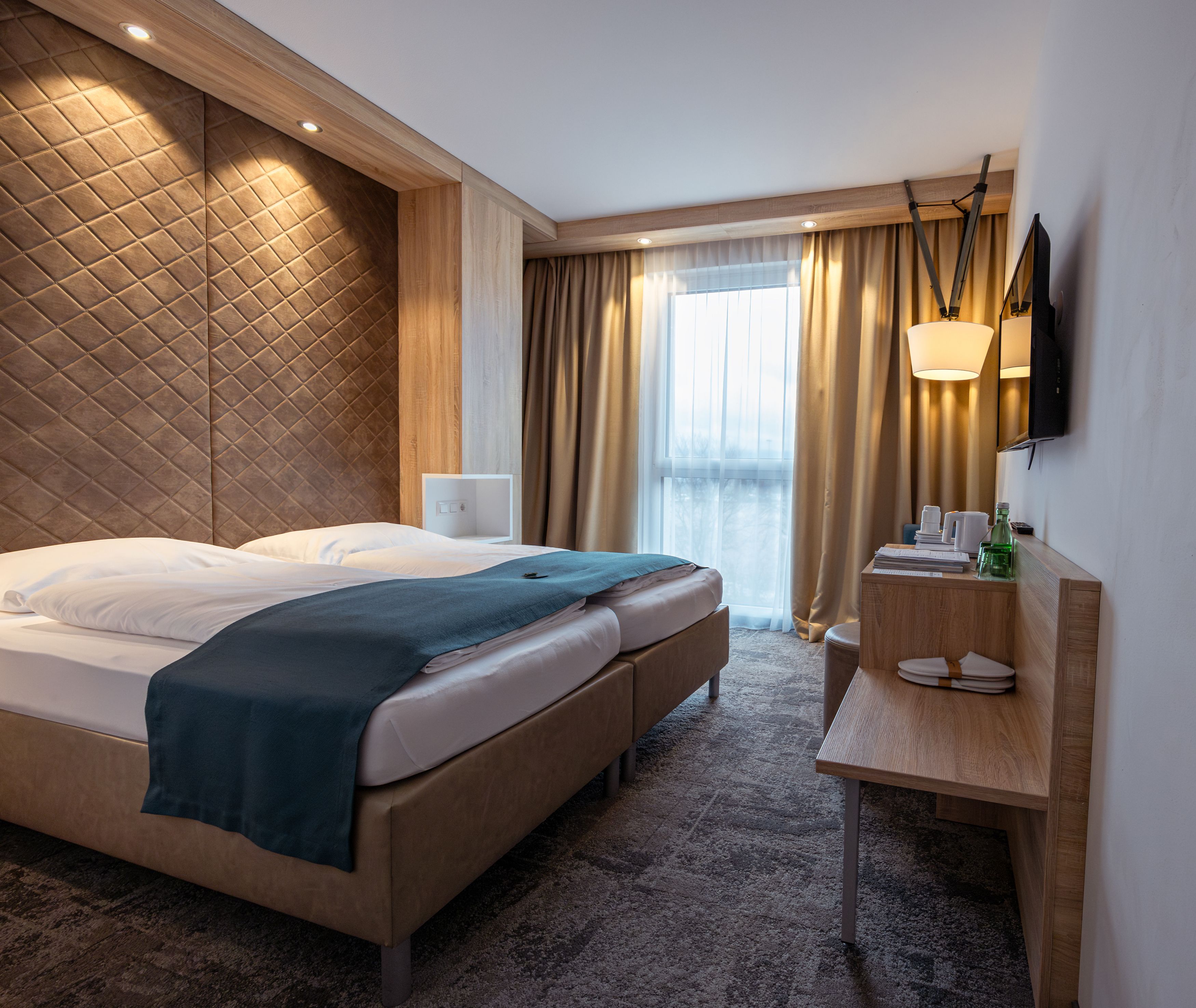 Modern hotel room with double bed, wooden paneling and windows with curtains.