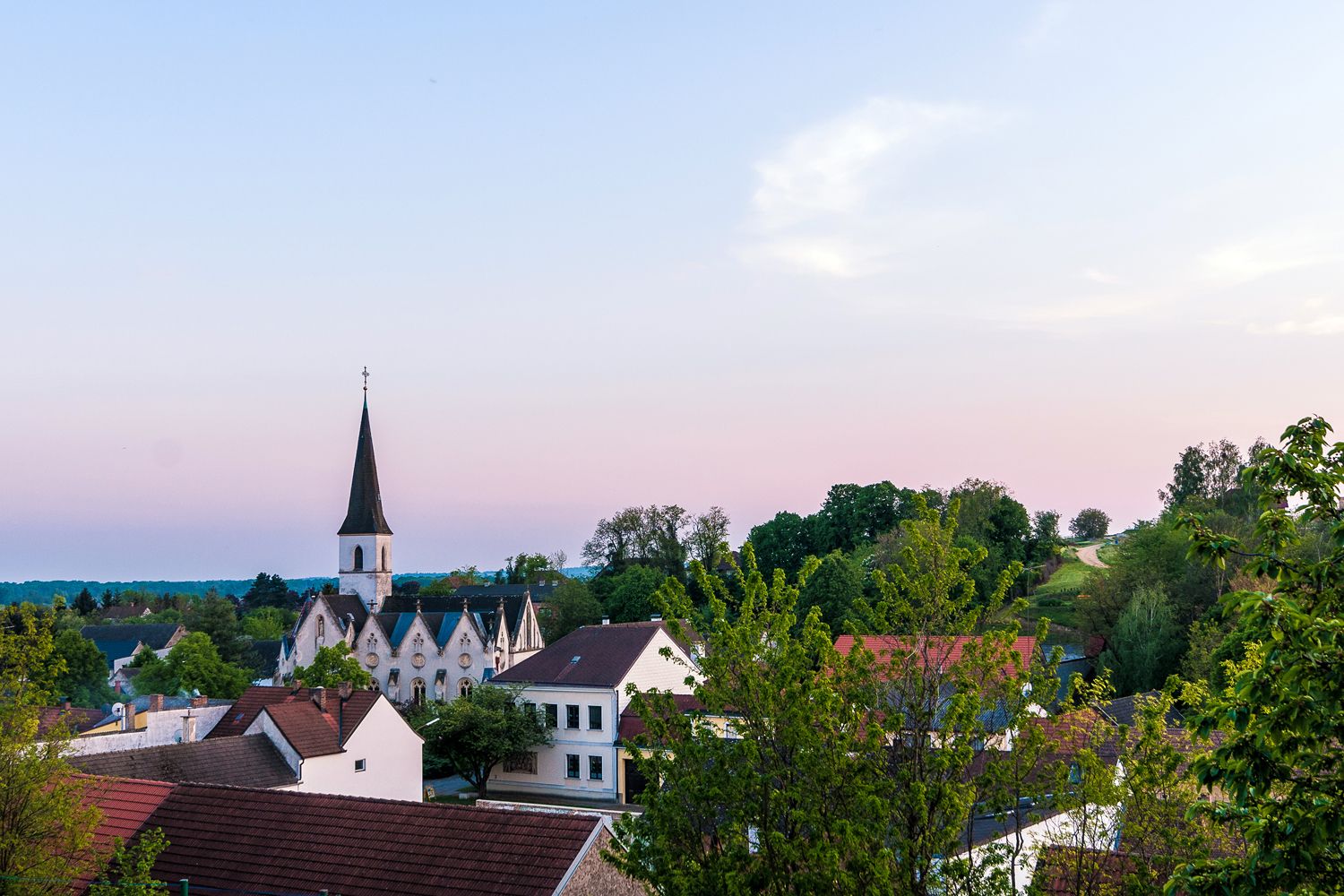 View of the Jedenspeigen church at sunset, surrounded by trees and houses.