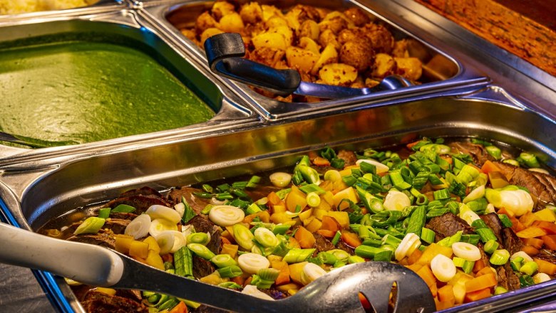 Buffet with various dishes in stainless steel containers.