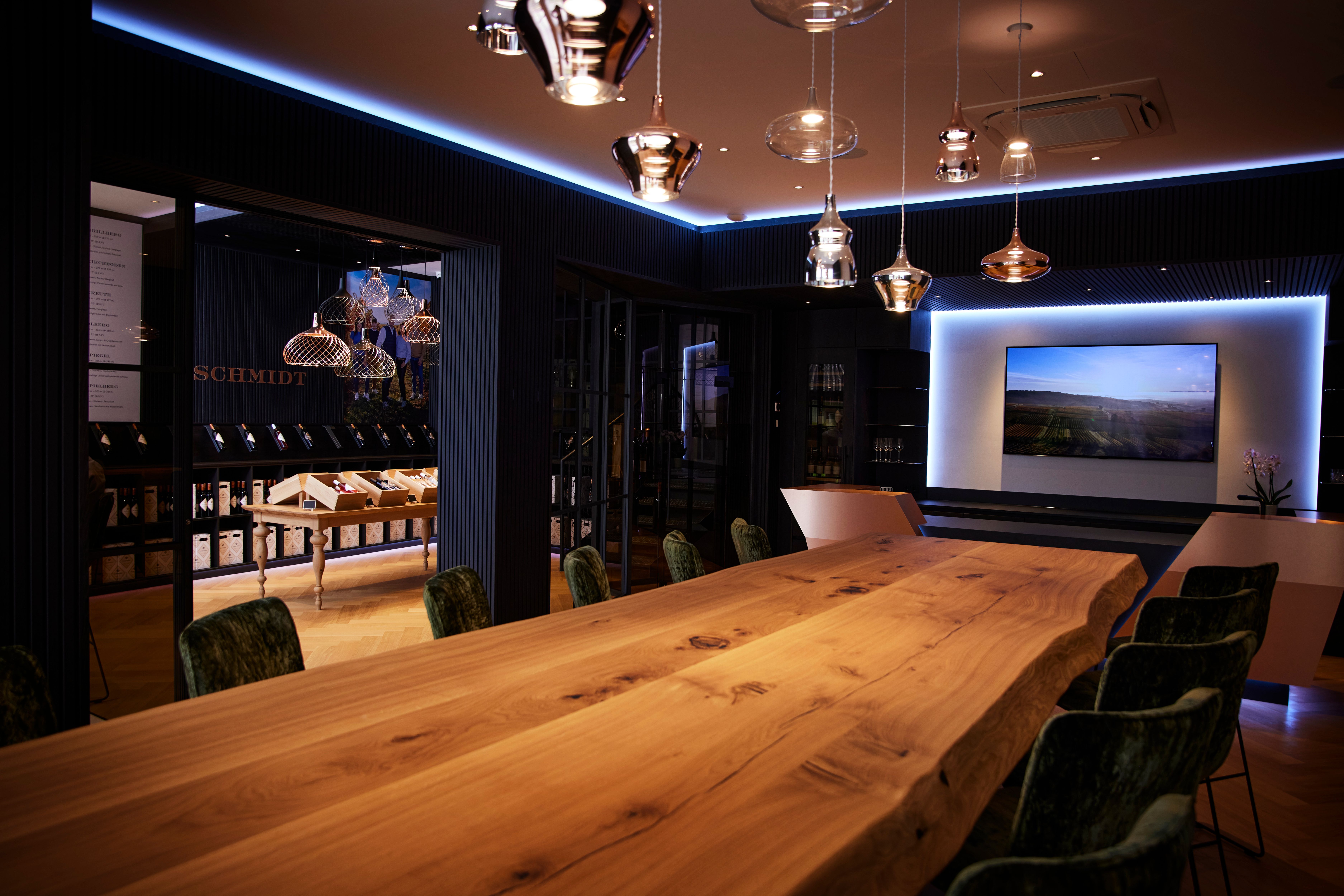 Elegant room with a long wooden table, modern lamps and a screen on the wall.