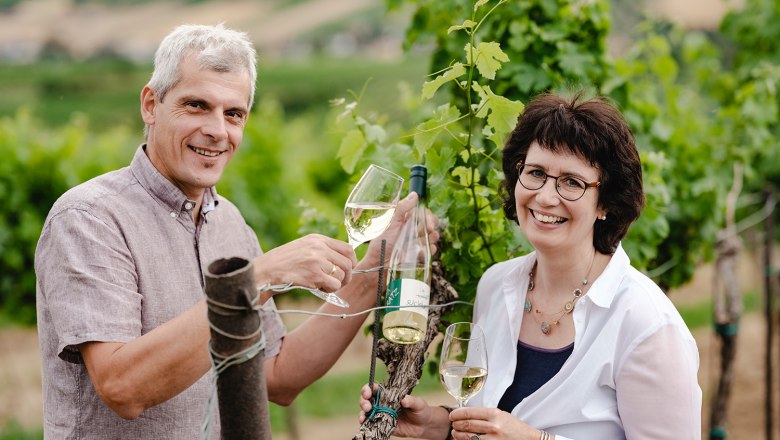 Two people clink glasses in a vineyard.
