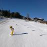Skiers on a sunny slope in Mönichkirchen with chair lift and snow cannons.