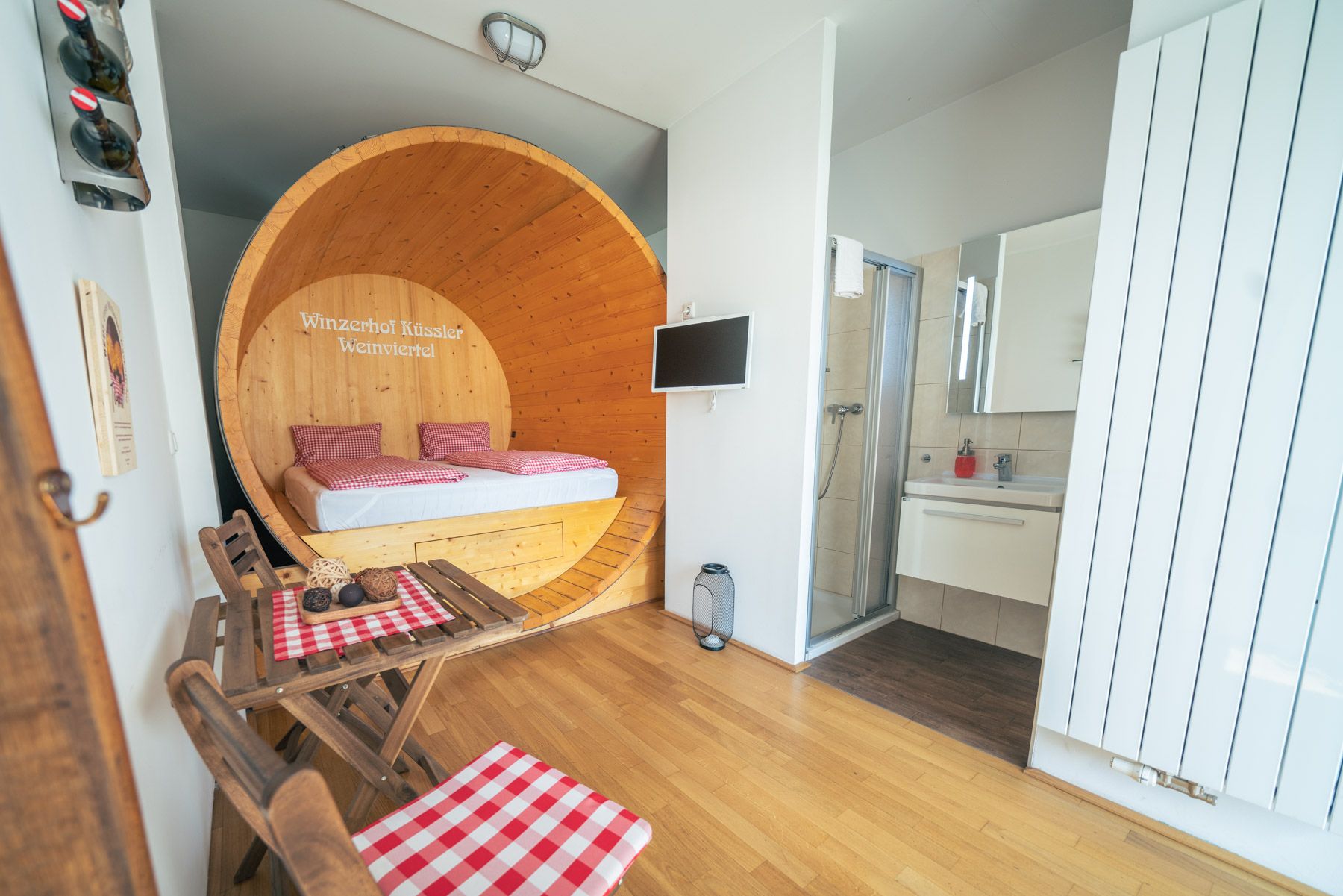 Interior view of a suite with a bed in a large wine barrel, a small table with chairs and a bathroom.