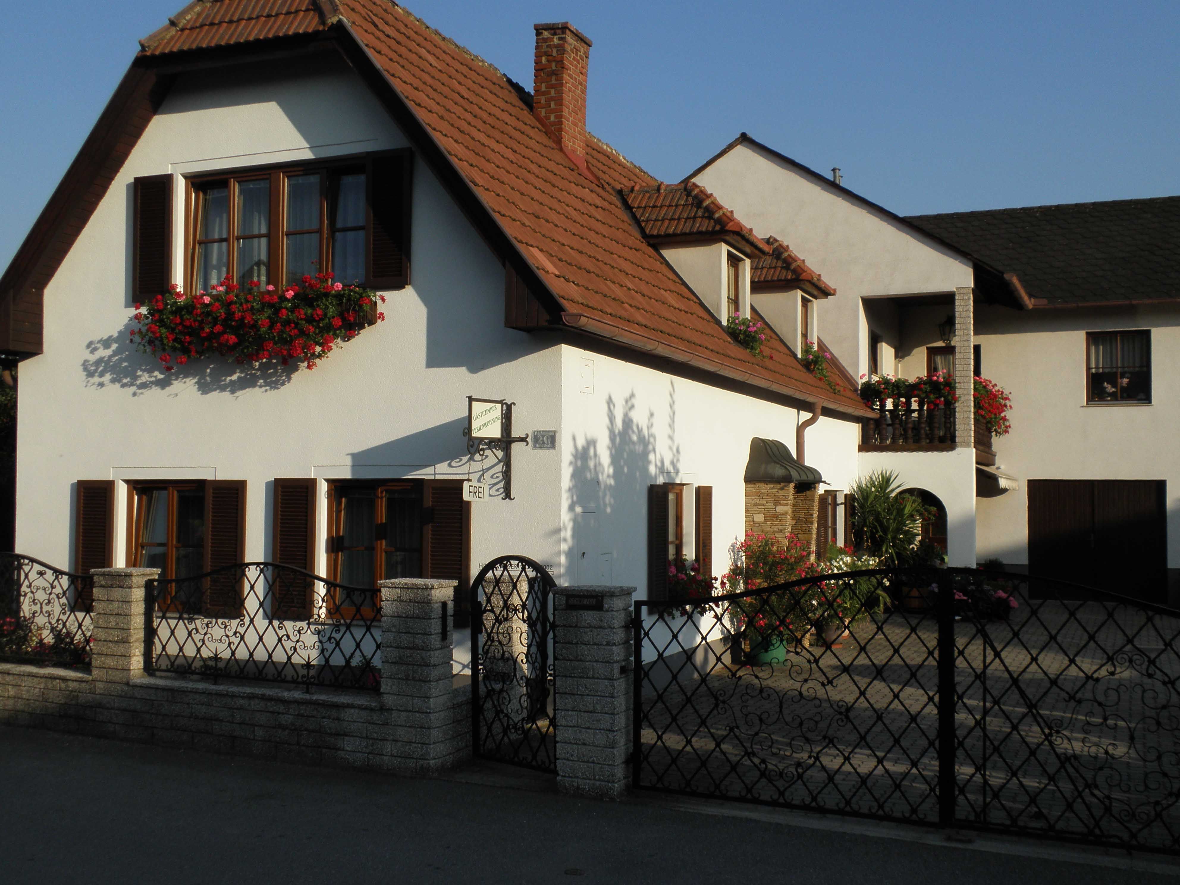 A two-storey house with white walls, red roof tiles and flower boxes in front of the windows.