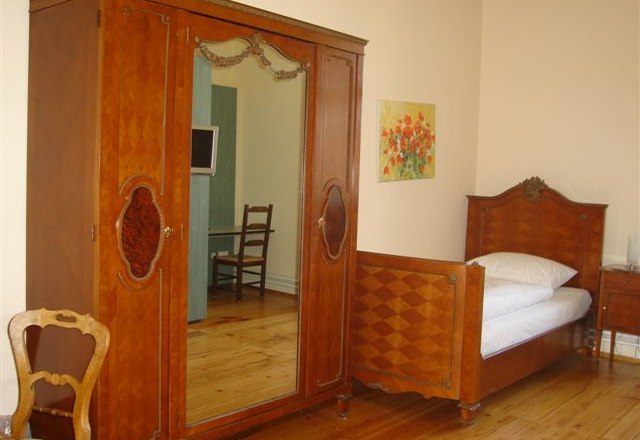 A traditionally furnished room with a wooden wardrobe, single bed and chair.
