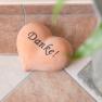Heart-shaped stone with the inscription 'Thank you' on tiled floor next to plant pot.