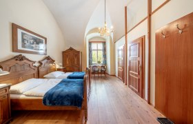 An elegant double room with antique wooden furniture, a chandelier and a window with a view of the greenery.
