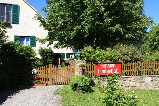 A house with a garden and a "Pension Lindenhof" sign on the wooden fence.