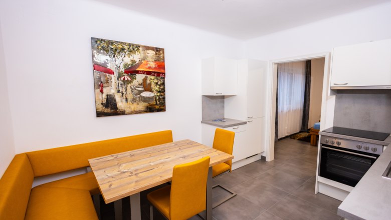 Modern kitchen with yellow corner bench, wooden table and artwork on the wall.