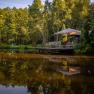 A peaceful pond with trees and a wooden deck with parasol and chairs.