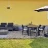 Terrace with yellow house wall, gray seating furniture, dining table, chairs and parasol.