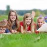Four children are lying in a meadow next to a white chicken.