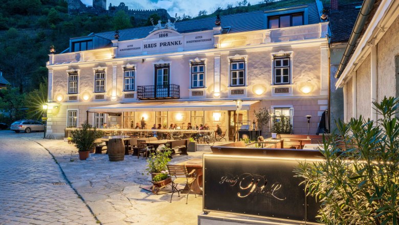 Exterior view of Gasthof Prankl at dusk with illuminated terrace and castle in the background.