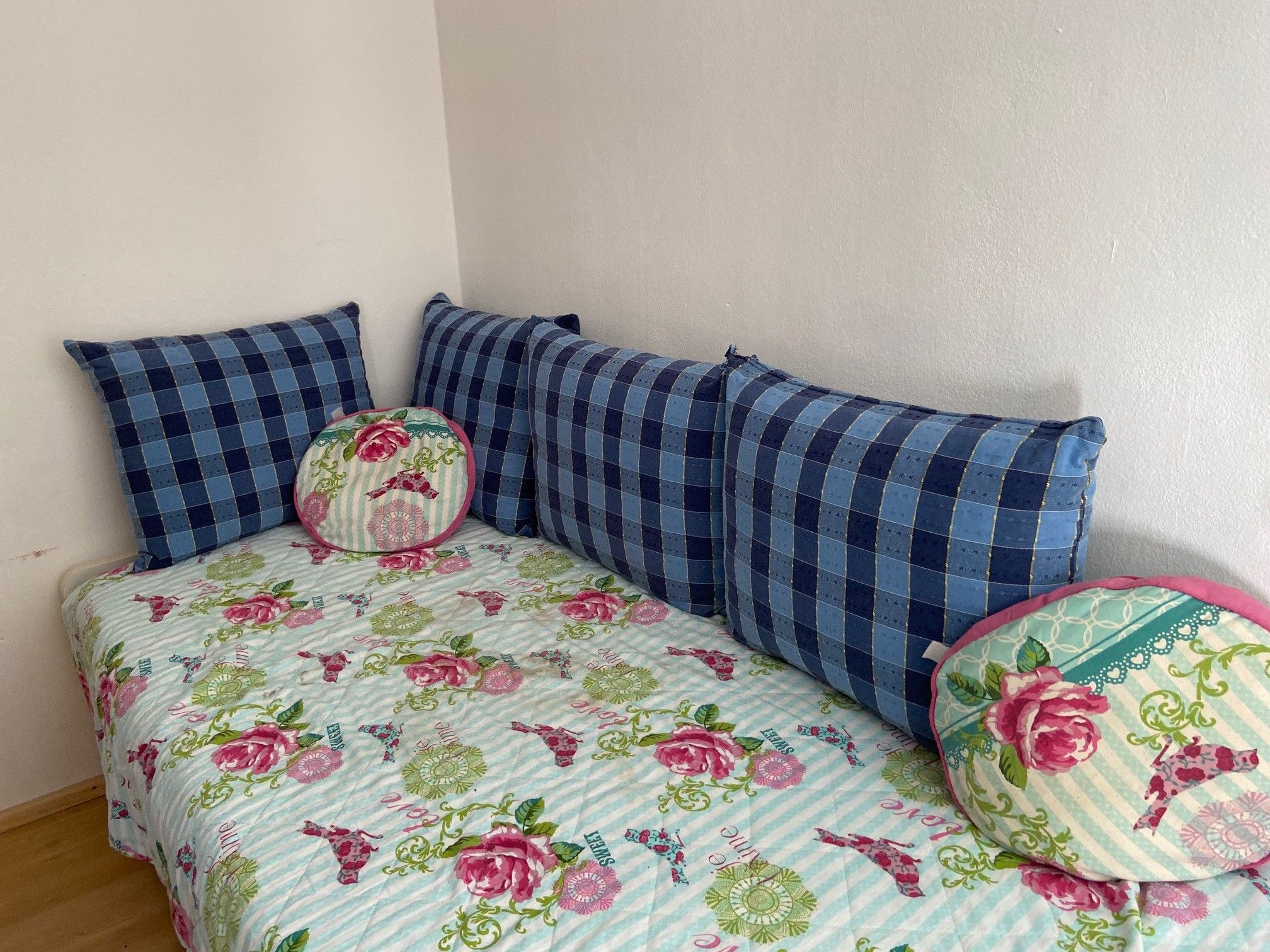 A children's room with a pull-out bed decorated with a flowered blanket and blue cushions.