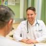 A doctor in a white coat smiles at a patient as they sit at a table.