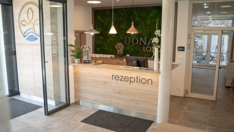 Reception with wooden counter and green moss wall in the background.