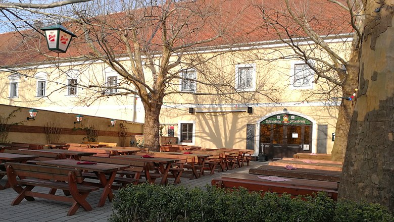 Beer garden with wooden benches and tables in front of a yellow building.